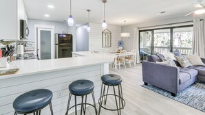 A modern kitchen with a white countertop, bar stools, and pendant lighting. - Walk to Coligny Beach: Tropical Hilton Head Condo (Hilton Head Island)