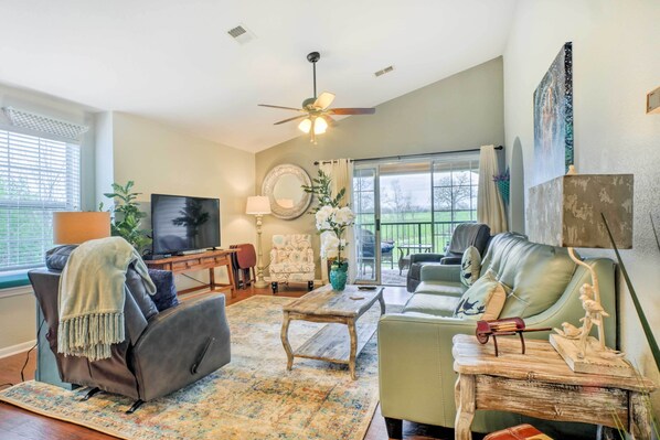 A living room with a ceiling fan, a television, a sofa, a coffee table, and a large window.