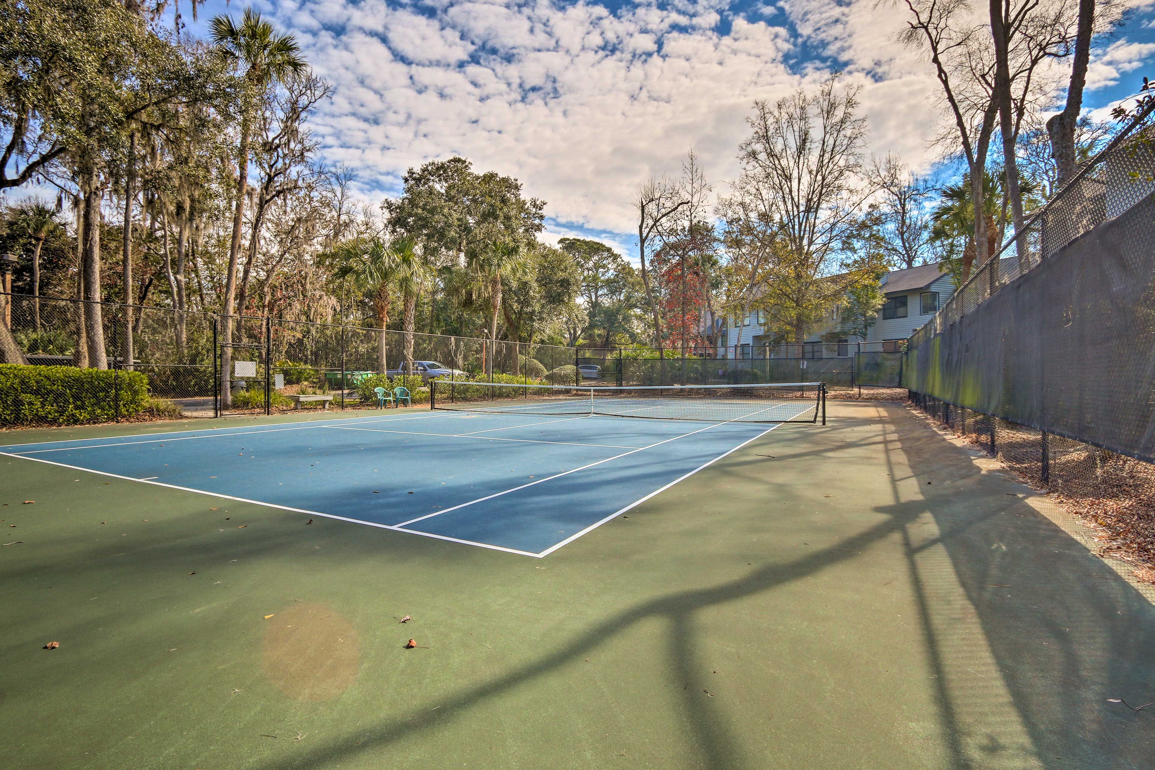 An outdoor tennis court surrounded by trees and a fence.