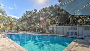 A clear swimming pool with a tiled deck, surrounded by trees and a covered area with lounge chairs. - Walk to Beach: HHI Townhome w/ Pool Access! (Hilton Head Island)
