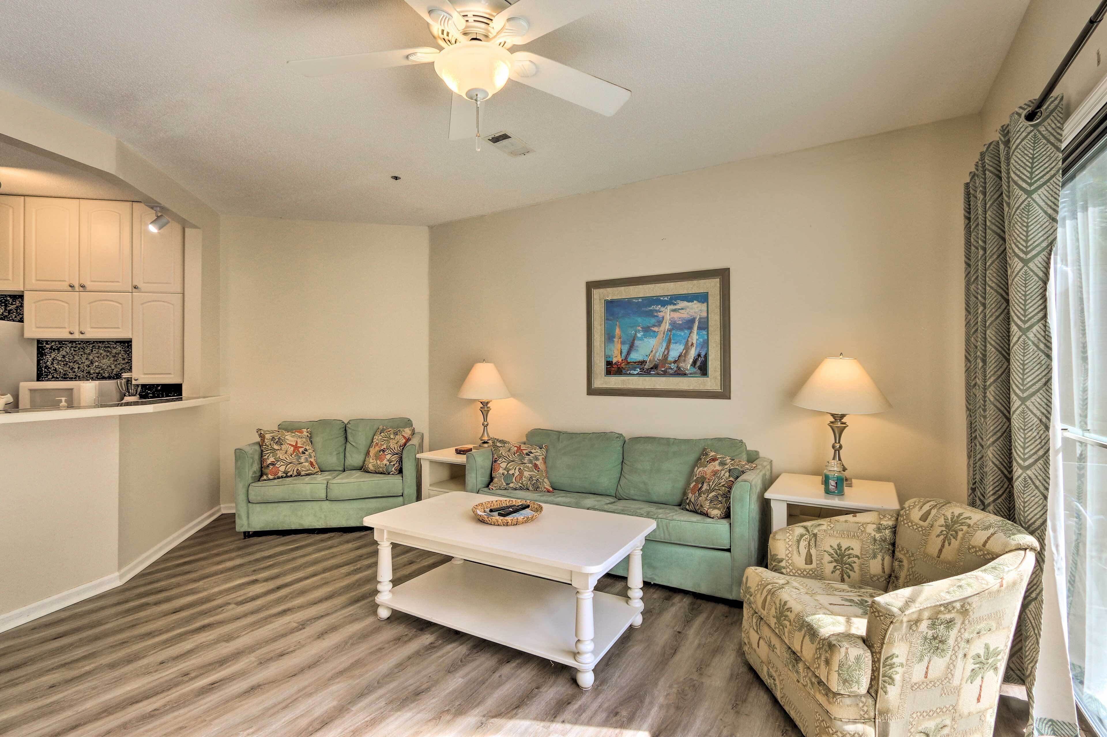 A living room with a green sofa, a patterned armchair, a white coffee table, and a ceiling fan.
