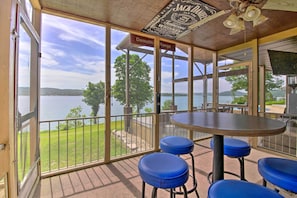 A covered outdoor seating area with a view of a lake, a sign for 'Demolition Range', and a ceiling fan. - Inviting Home w/ Pool & Hot Tub on Table Rock Lake (Lampe)