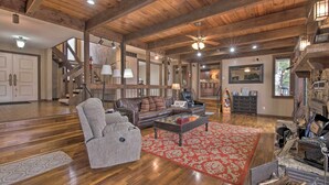 A spacious living room with a wooden ceiling, a fireplace, a sofa, a coffee table, and a red patterned rug. - Inviting Home w/ Pool & Hot Tub on Table Rock Lake (Lampe)