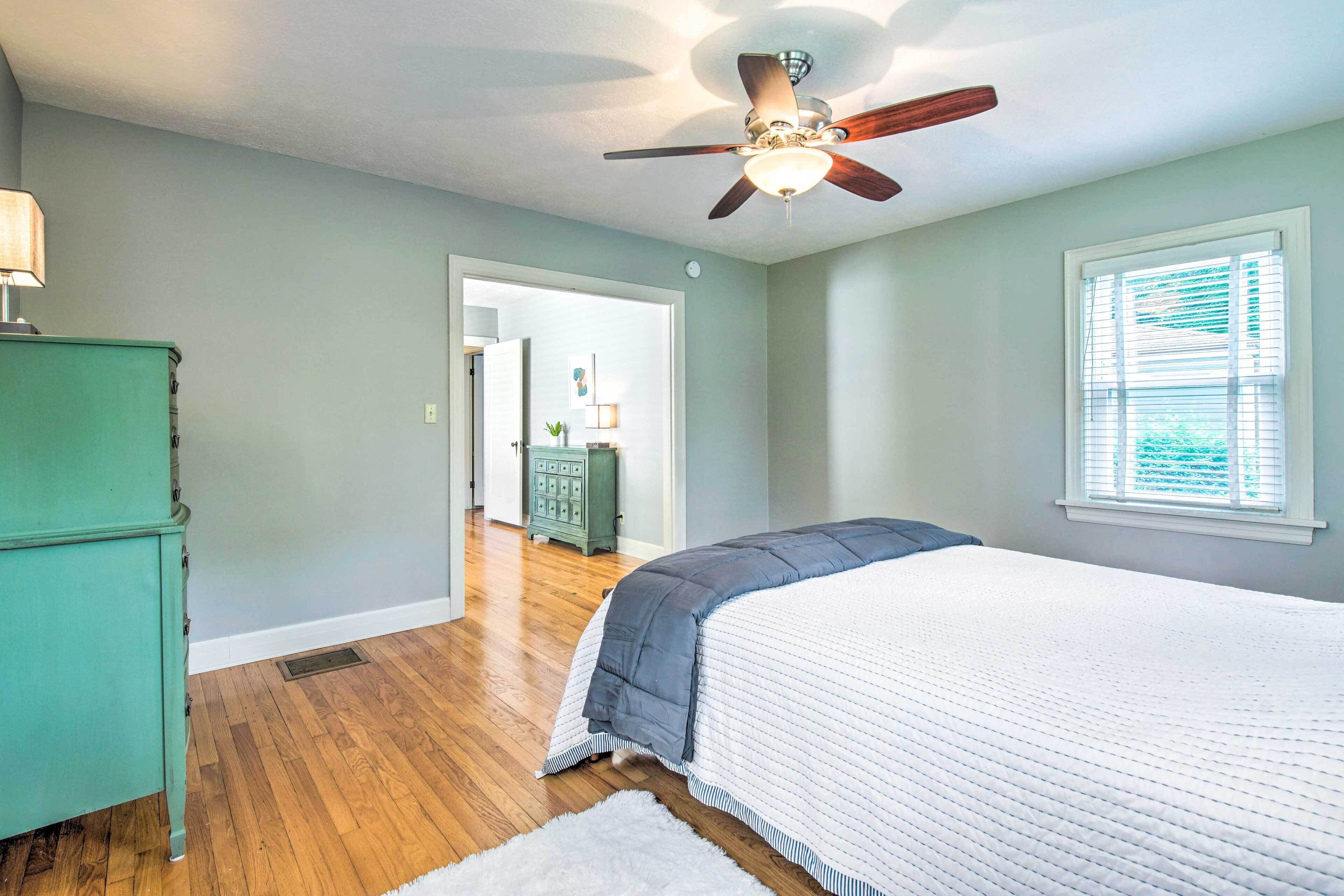 A bedroom with a bed, a ceiling fan, a window with blinds, and a wooden floor.