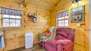 A cozy cabin interior with wooden walls, a red sofa, a window with curtains, and a welcome sign. - Creek Views & Grill: Idyllic Florence Cabin (Florence)