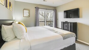 Une chambre à coucher avec un lit, un ventilateur de plafond, une télévision, une fenêtre avec des rideaux et un tableau encadré au mur.