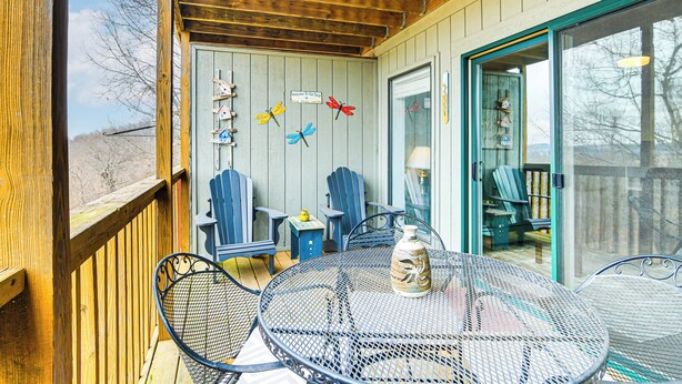 Une terrasse couverte avec une table ronde en métal, des chaises bleues et une plateforme en bois.