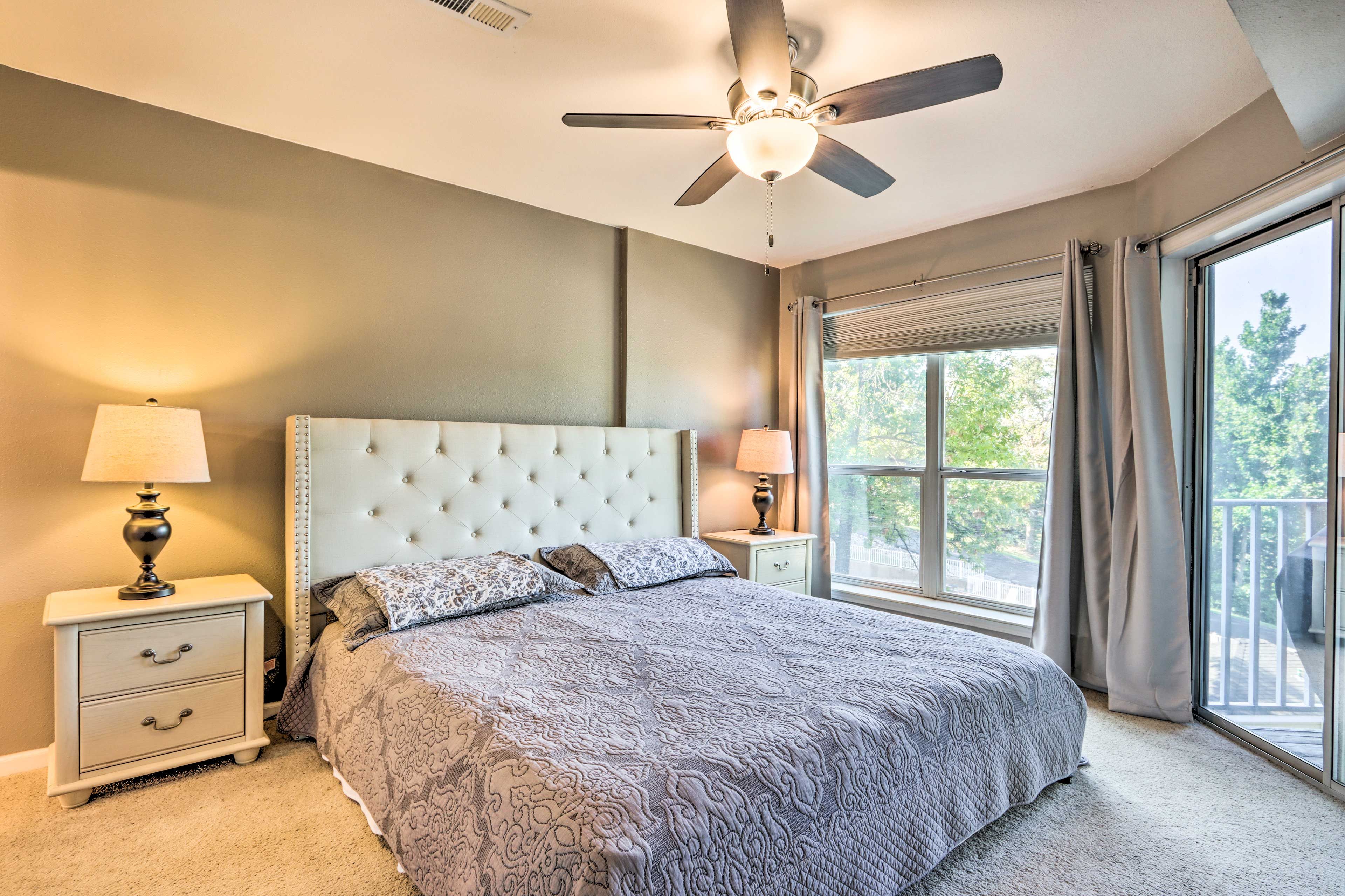 A bedroom with a tufted headboard, two bedside tables with lamps, a large window with curtains, and a ceiling fan.