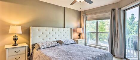 A bedroom with a tufted headboard, two bedside tables with lamps, a large window with curtains, and a ceiling fan.