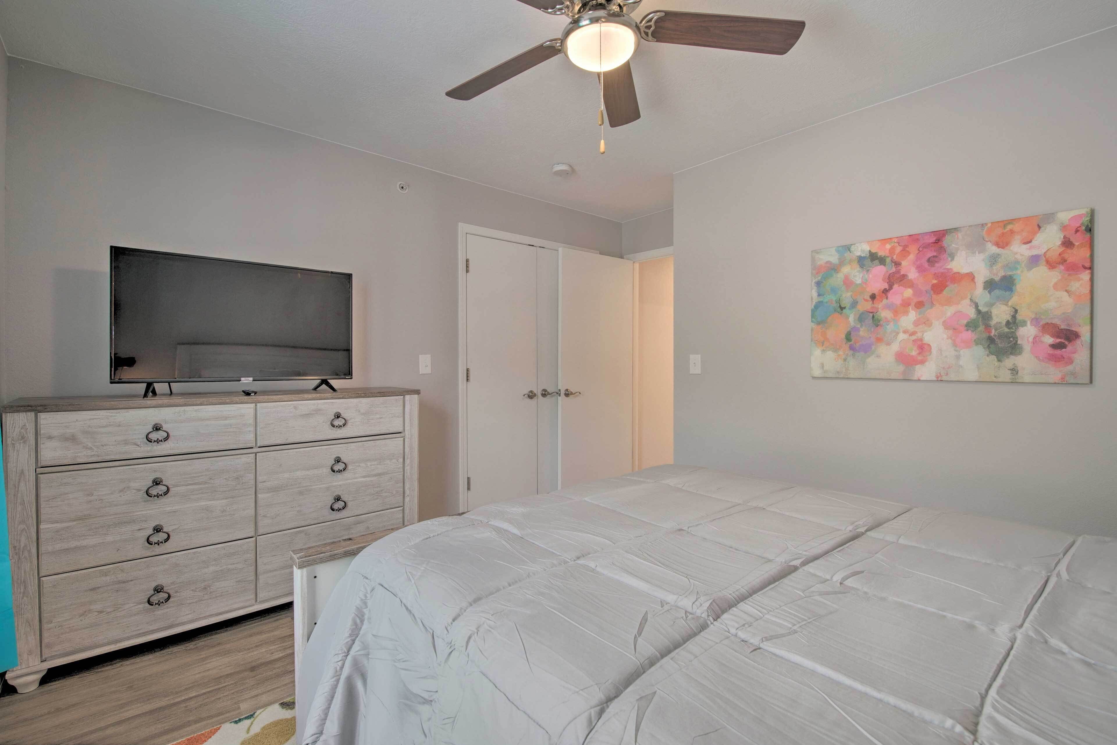 A bedroom with a bed, a dresser, a ceiling fan, a television, and a door.