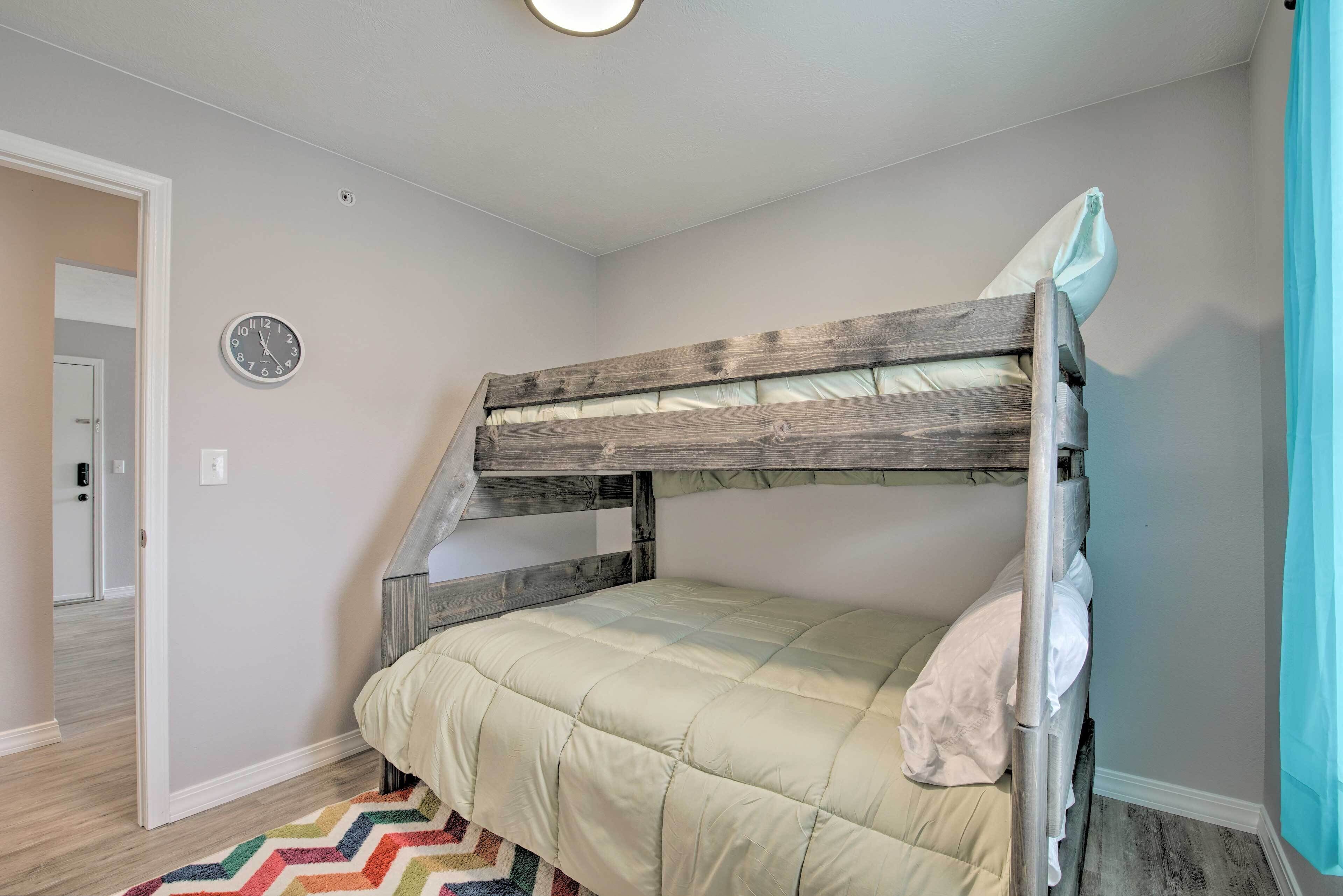 A bunk bed with a wooden frame and a quilted mattress, a clock on the wall, and a chevron-patterned rug.