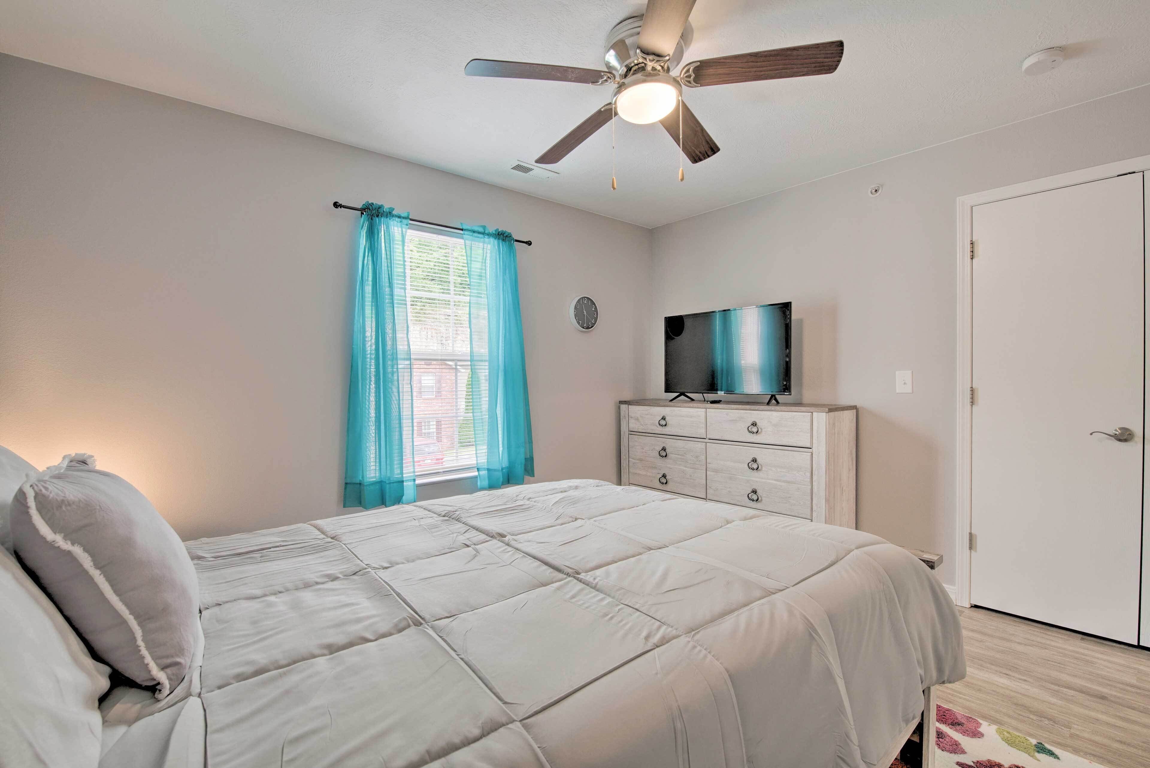 A bedroom with a bed, a ceiling fan, a dresser, a television, and a door.