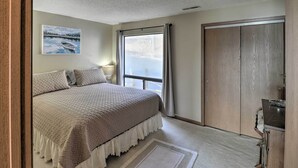 A bedroom with a large bed, a window with curtains, a wooden wardrobe, and a painting on the wall. - Pool + Fishing Docks: Couple's Lake Ozark Condo (Lake Ozark)