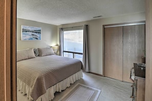 A bedroom with a large bed, a window with curtains, a wooden wardrobe, and a painting on the wall. - Pool + Fishing Docks: Couple's Lake Ozark Condo (Lake Ozark)