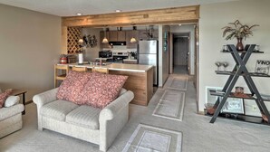 A modern living room with a sofa and a coffee table, a kitchen with wooden cabinets and stainless steel appliances, and a hallway leading to another room. - Pool + Fishing Docks: Couple's Lake Ozark Condo (Lake Ozark)