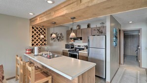 A modern kitchen with a large island, wooden cabinets, stainless steel appliances, pendant lighting, and a built-in wine rack. - Pool + Fishing Docks: Couple's Lake Ozark Condo (Lake Ozark)