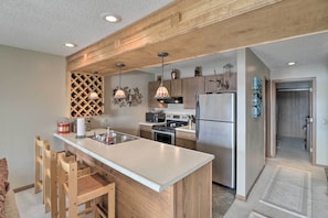A modern kitchen with a large island, wooden cabinets, stainless steel appliances, pendant lighting, and a built-in wine rack. - Pool + Fishing Docks: Couple's Lake Ozark Condo (Lake Ozark)