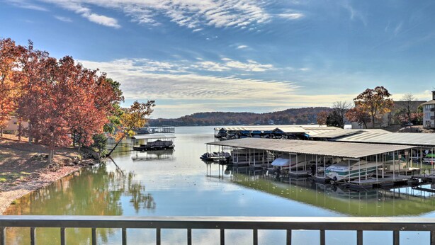 A marina with docked boats, a covered boat house, and autumn trees reflecting on the water. - Pool + Fishing Docks: Couple's Lake Ozark Condo (Lake Ozark)