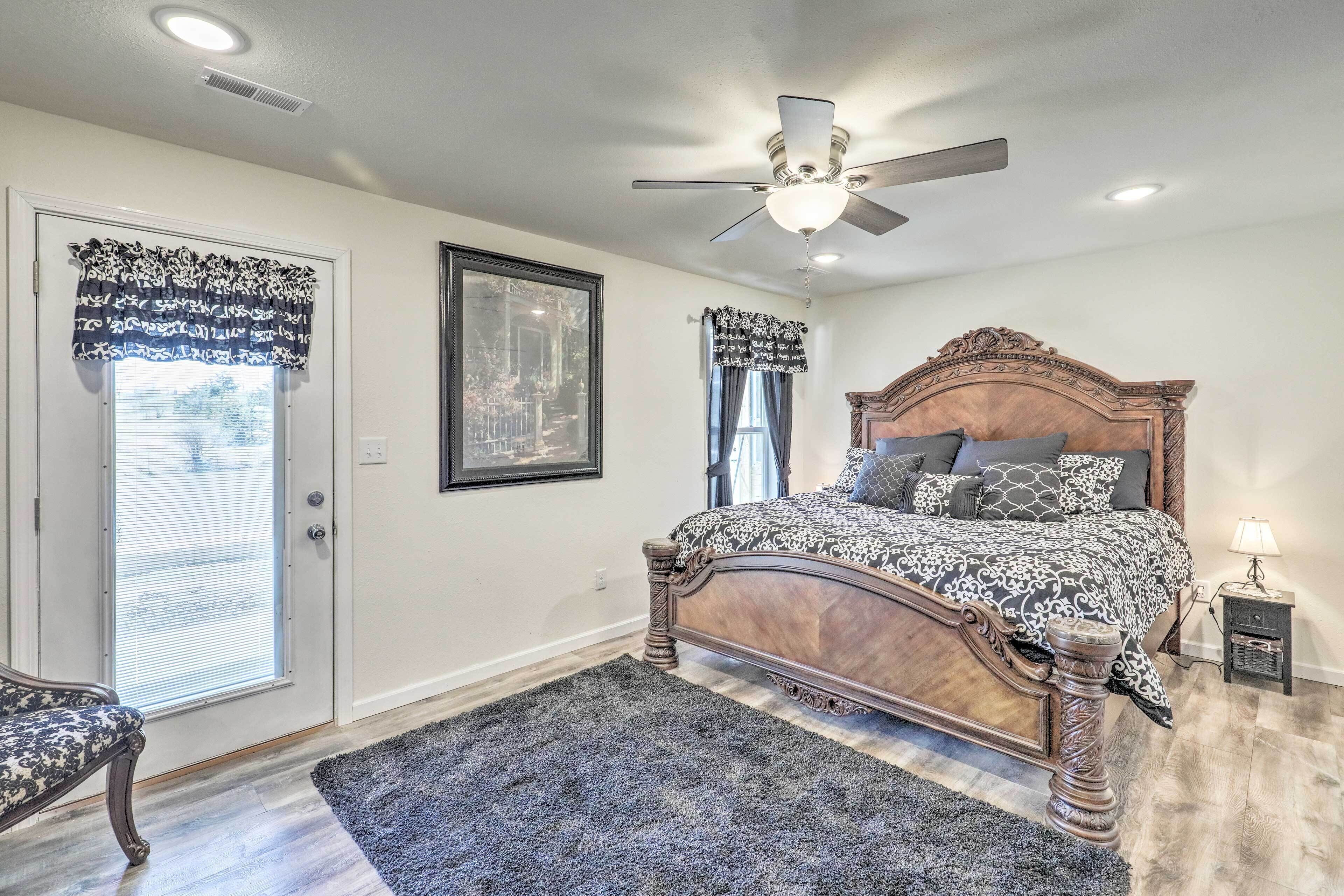 A bedroom with a wooden bed, a ceiling fan, a framed picture on the wall, and a door with patterned curtains.
