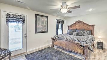 A bedroom with a wooden bed, a ceiling fan, a framed picture on the wall, and a door with patterned curtains.