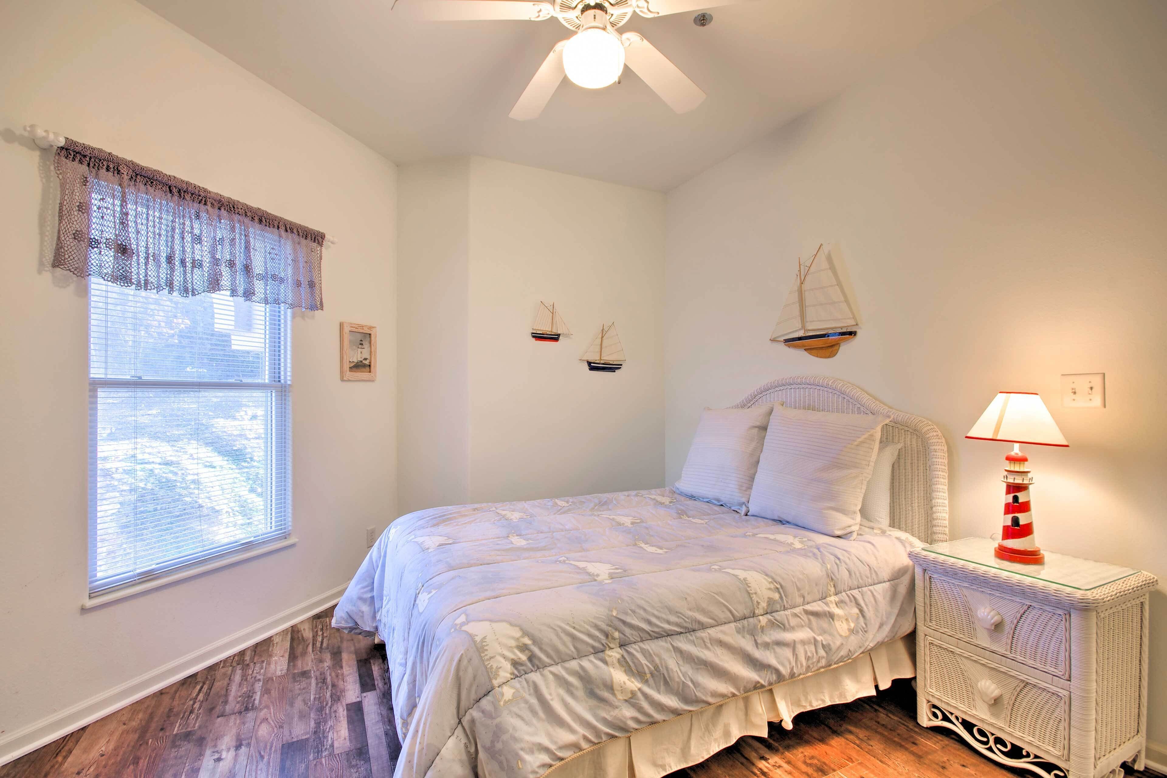 A bedroom with a bed, a nightstand, a window with blinds, and a ceiling fan.