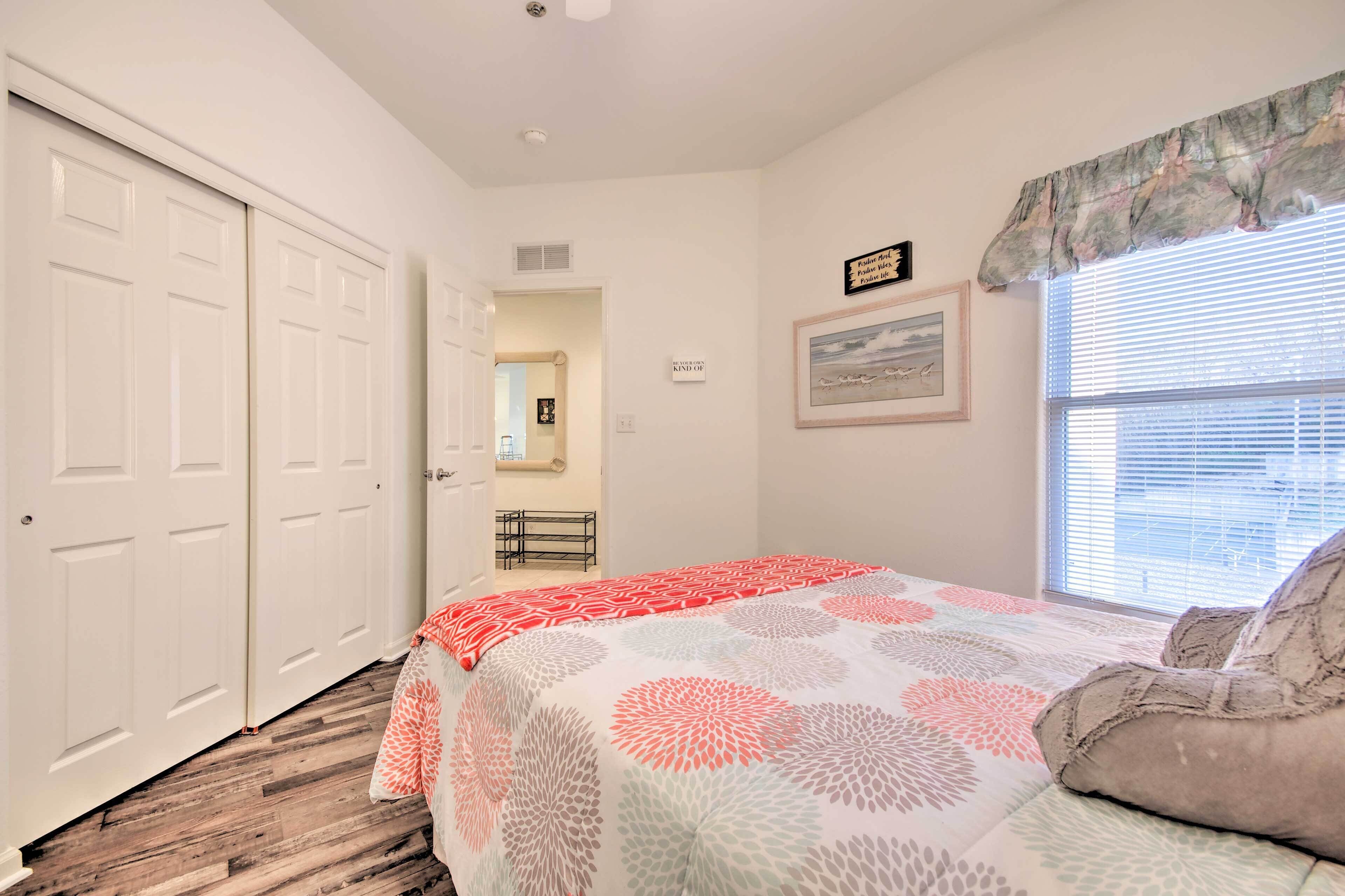 A bedroom with a bed, a window with blinds, a door, and a wall with a framed picture and a sign.