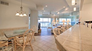 Une cuisine spacieuse avec un grand îlot central, des chaises en osier et des luminaires suspendus.