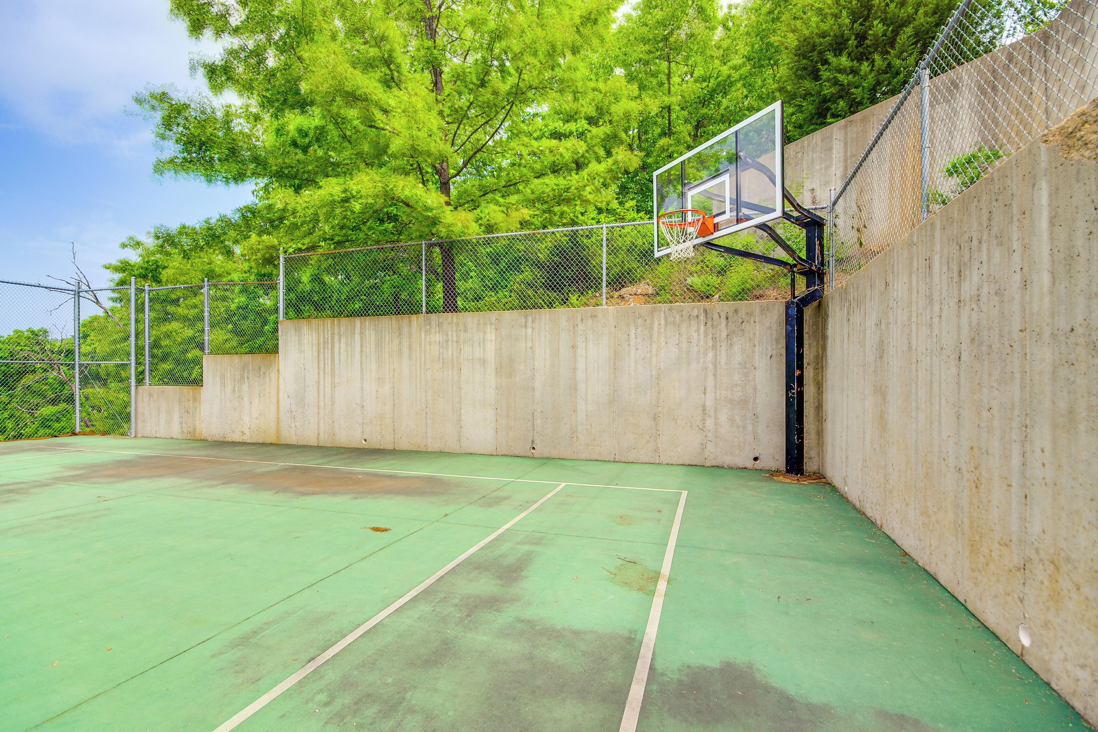 An outdoor basketball court with a chain-link fence, a basketball hoop, and a concrete wall.