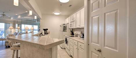 A modern kitchen with white cabinets, a large island with bar stools, and a view of the ocean through large windows.