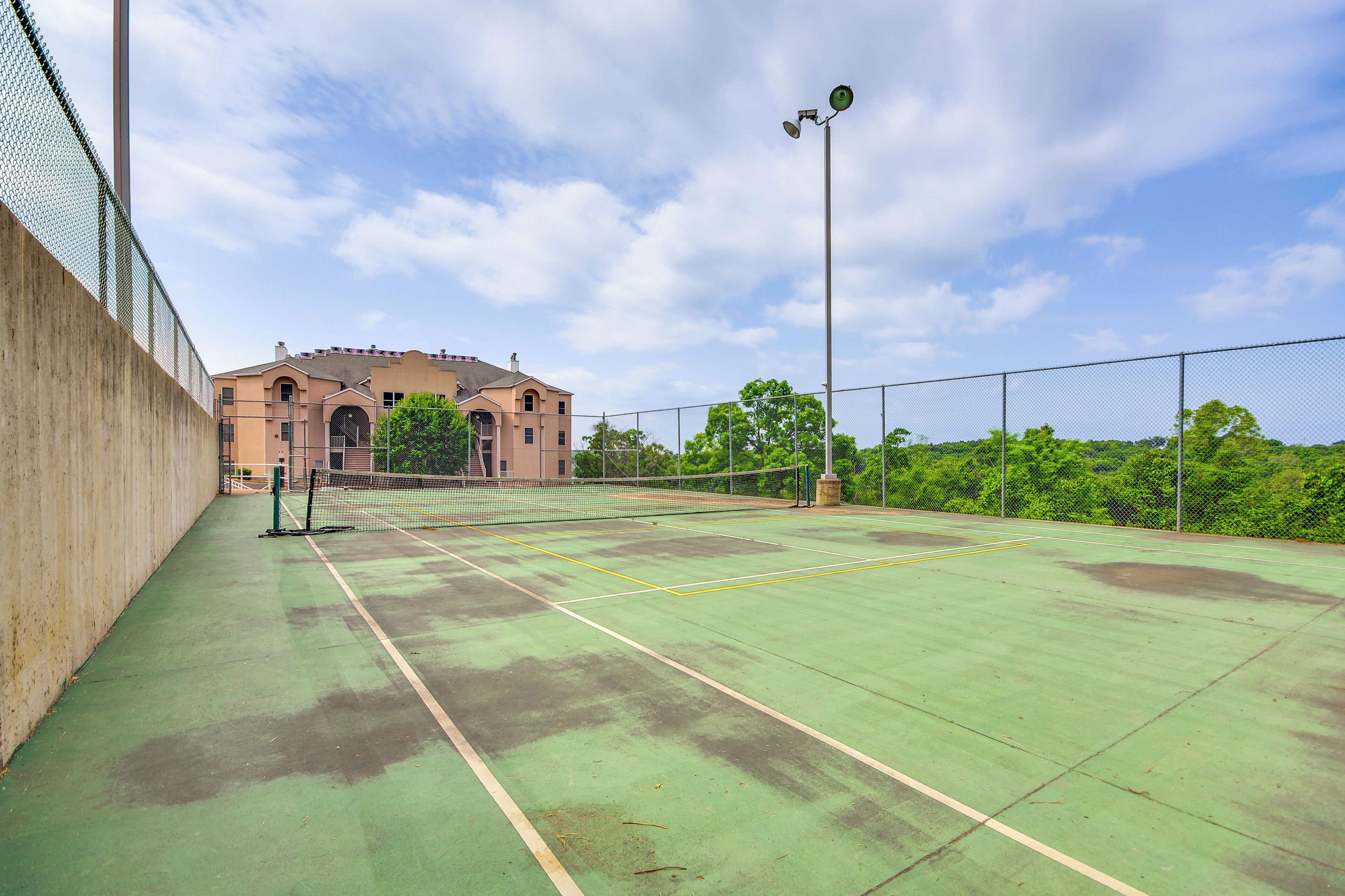 En utomhusbana för tennis med ett nät, omgiven av ett staket, och en byggnad i bakgrunden.