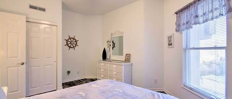 A bedroom with a bed, a dresser, a ceiling fan, a window with blinds, and a door.