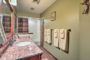 A bathroom with a granite sink, a mirror, a towel rack with towels, a shower, and a framed picture on the wall. - Kimberling City Home w/ Table Rock Lake Views! (Kimberling City)