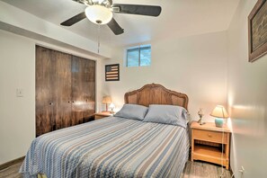 A bedroom with a bed, wooden wardrobe, ceiling fan, nightstands with lamps, and a small window. - Kimberling City Home w/ Table Rock Lake Views! (Kimberling City)