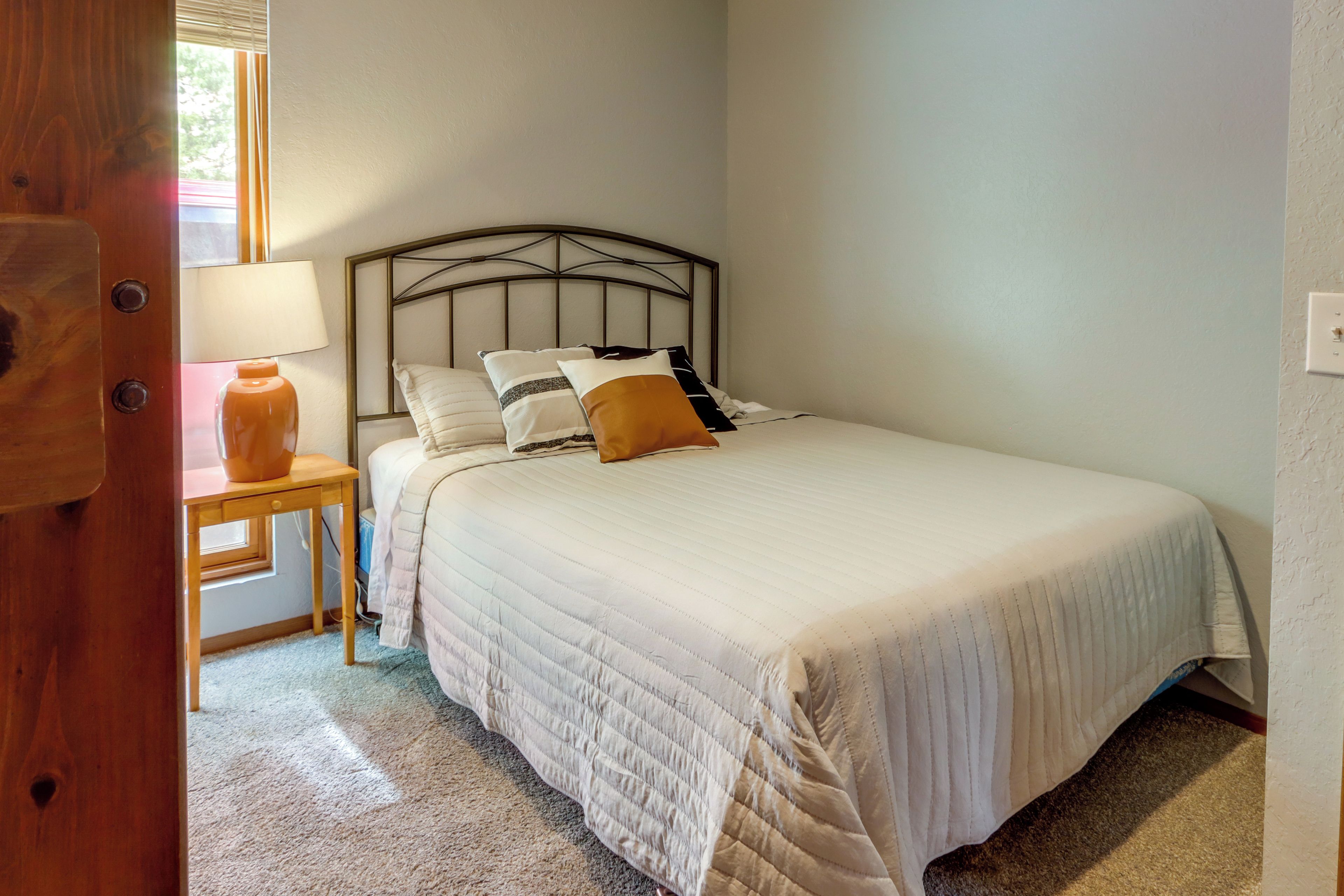 A neatly made bed with a headboard, a bedside table with a lamp, and a small window with blinds.