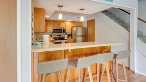 A kitchen with wooden cabinets, a stainless steel refrigerator, and a bar area with wicker chairs. - Oasis at Spring Valley Cove, Quiet, Private Dock (Osage Beach)