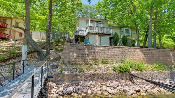 A two-story house with a balcony, surrounded by trees and a small stream. - Oasis at Spring Valley Cove, Quiet, Private Dock (Osage Beach)