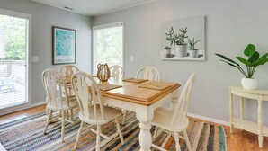 A dining area with a wooden table and white chairs, a colorful rug, and a potted plant on a small table. - Oasis at Spring Valley Cove, Quiet, Private Dock (Osage Beach)