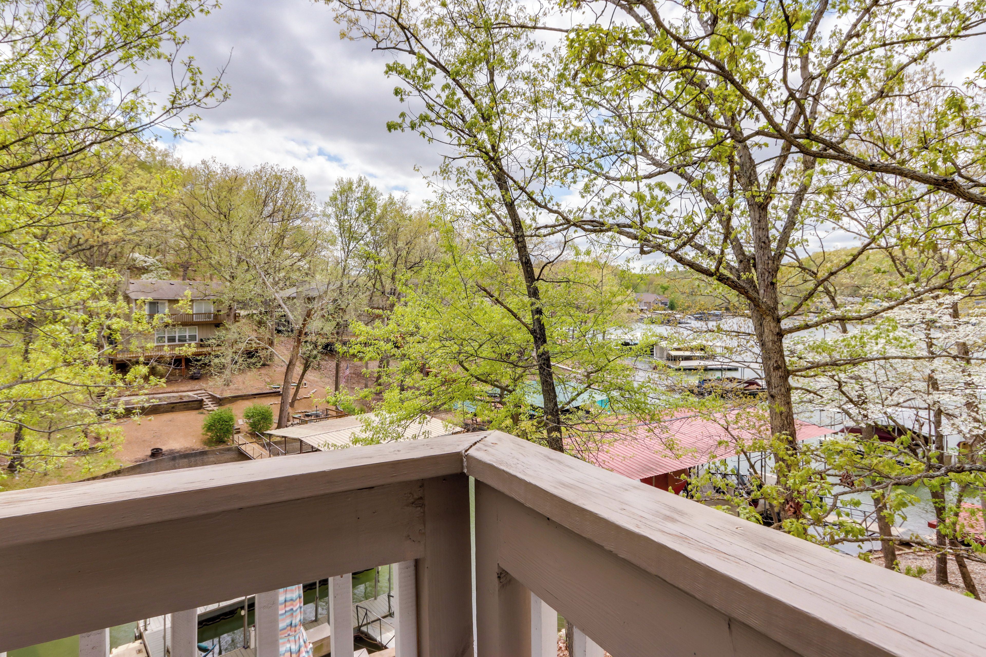 A view from a balcony overlooking a residential area with houses, trees, and a body of water.