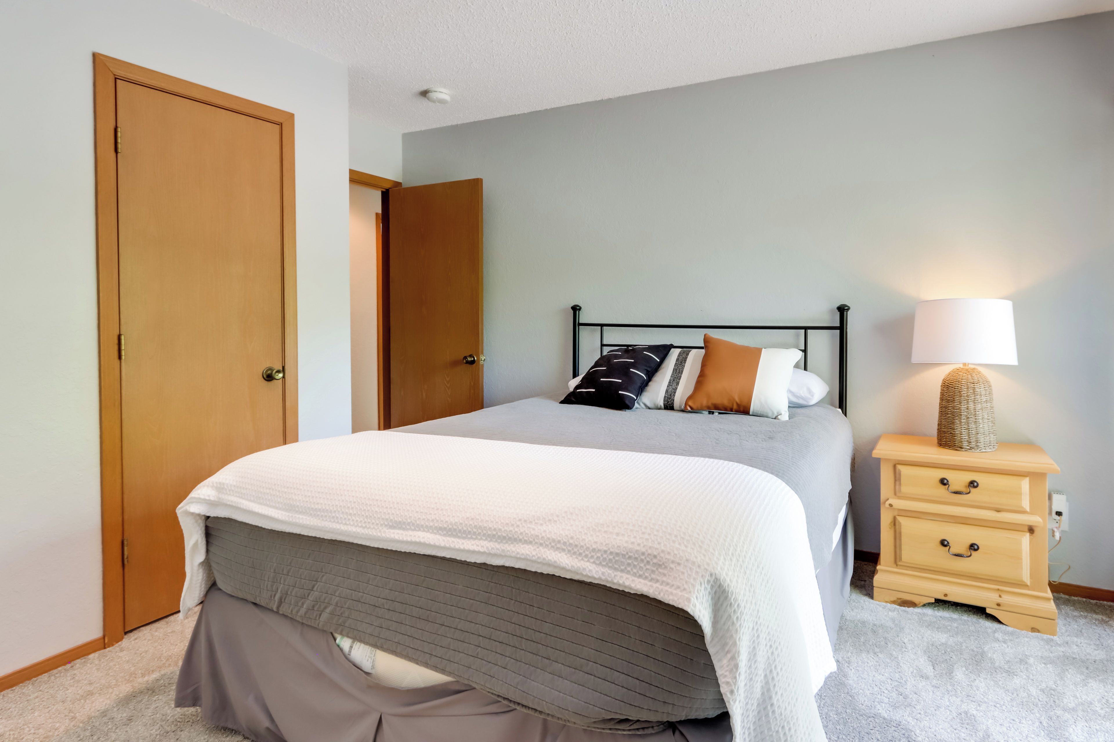 Un dormitorio con cama, mesita de noche, lámpara y puerta.