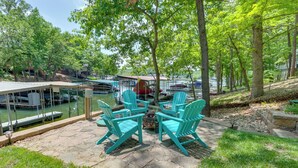 A patio area with turquoise chairs and a table, surrounded by trees and a dock with boats. - Oasis at Spring Valley Cove, Quiet, Private Dock (Osage Beach)