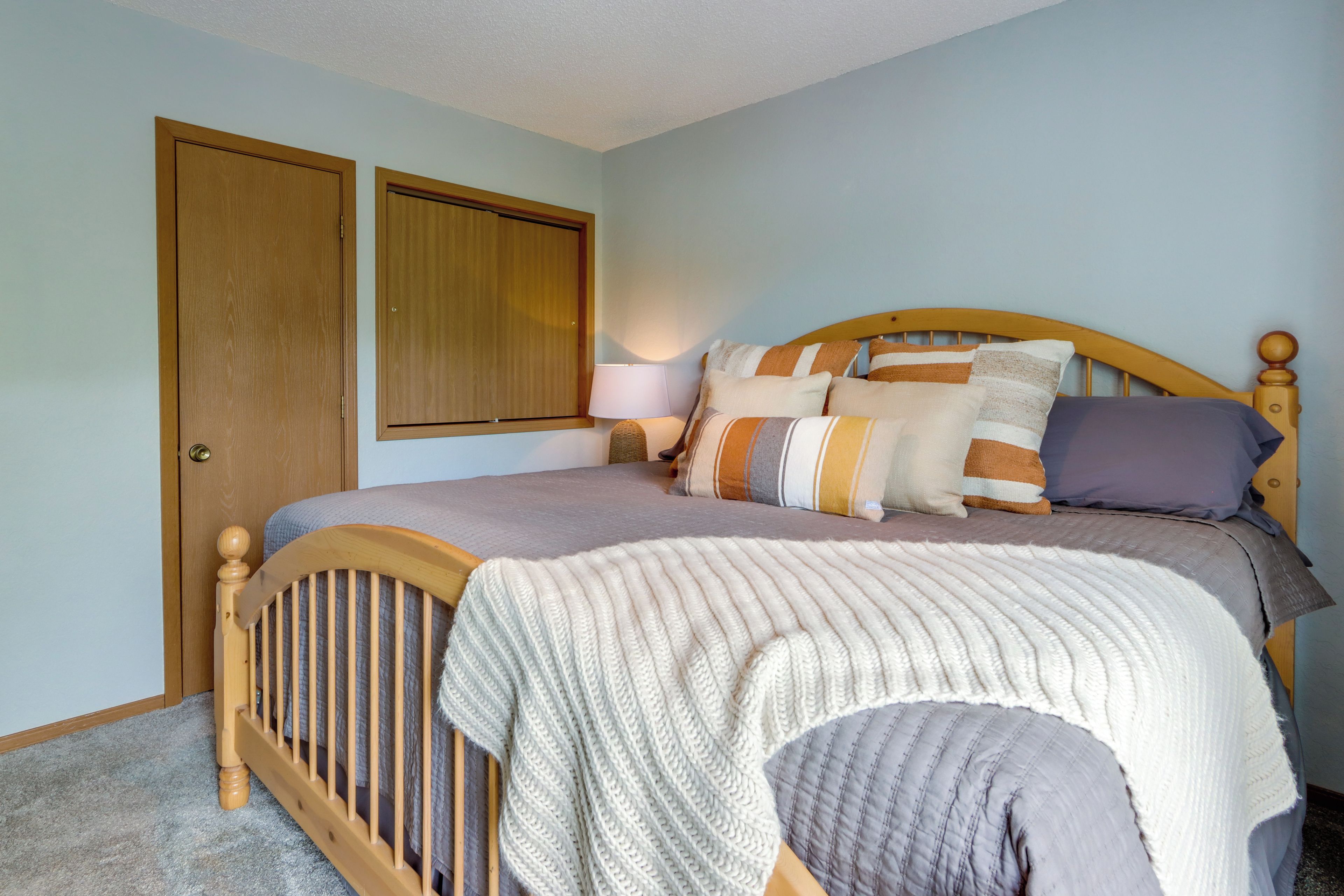Een slaapkamer met een houten bed, een nachtkastje, een lamp en twee deuren.