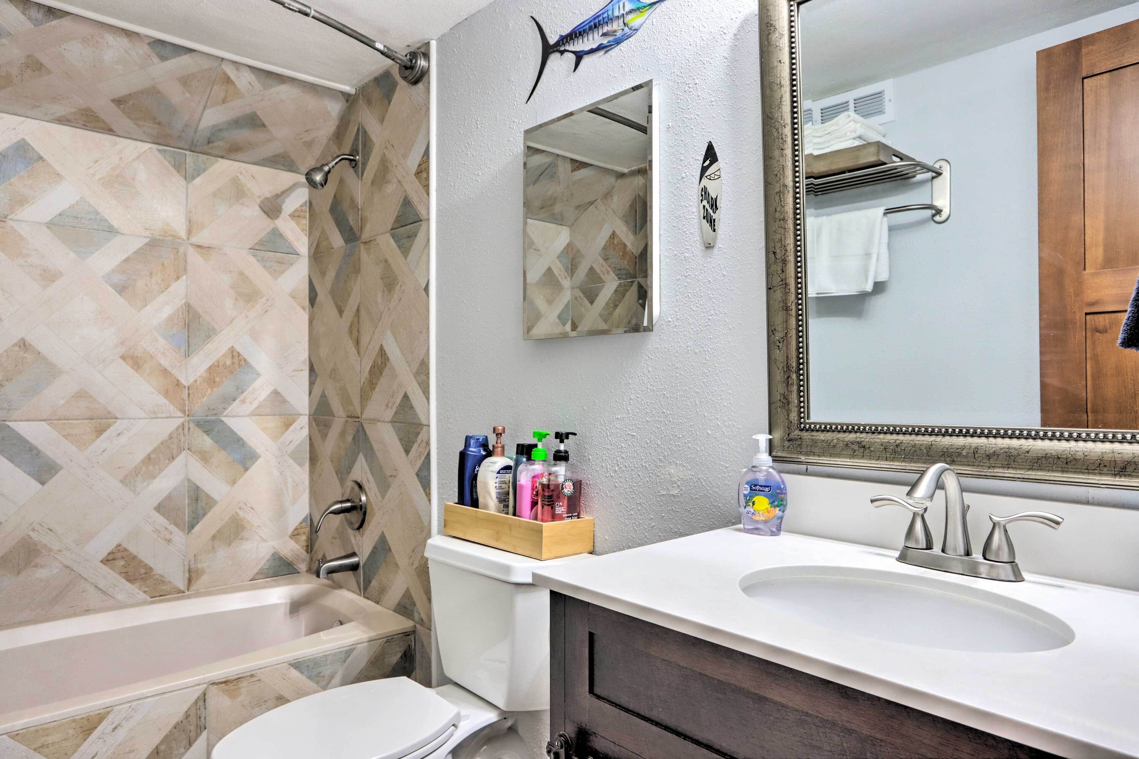 A bathroom with a bathtub, a sink, and a mirror. There are toiletries on the sink counter.