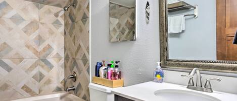 A bathroom with a bathtub, a sink, and a mirror. There are toiletries on the sink counter.