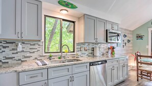 A modern kitchen with grey cabinets, a stainless steel dishwasher, and a large window.