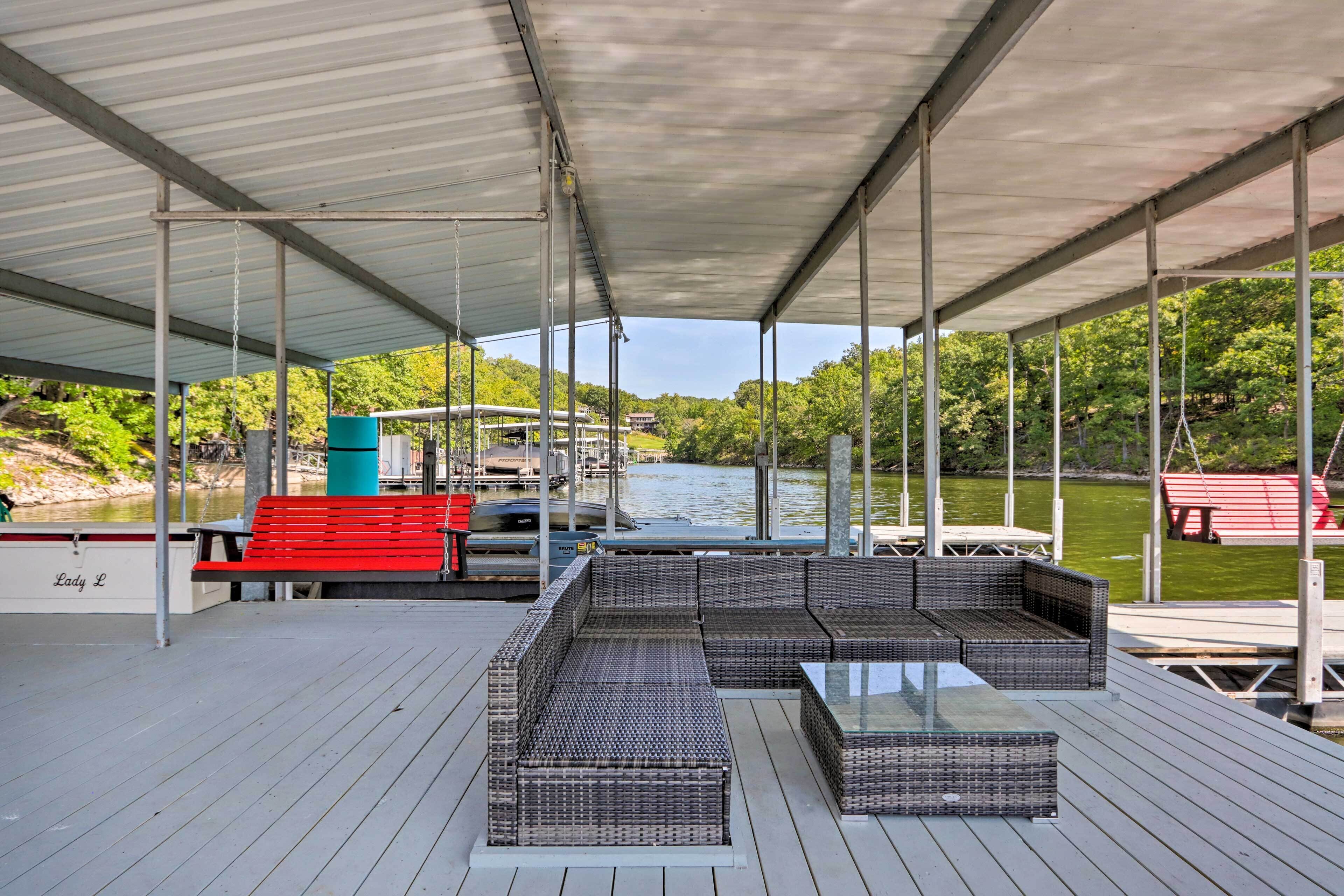 A covered deck with wicker furniture, a red bench, and a boat docked in the background.