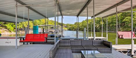 A covered deck with wicker furniture, a red bench, and a boat docked in the background.