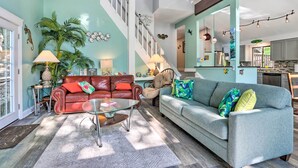 A spacious living room with a high ceiling, a staircase, a kitchen, and a dining area.