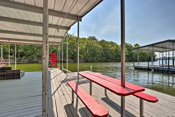Terraza de madera con mesas de picnic y una zona cubierta que da a un cuerpo de agua.