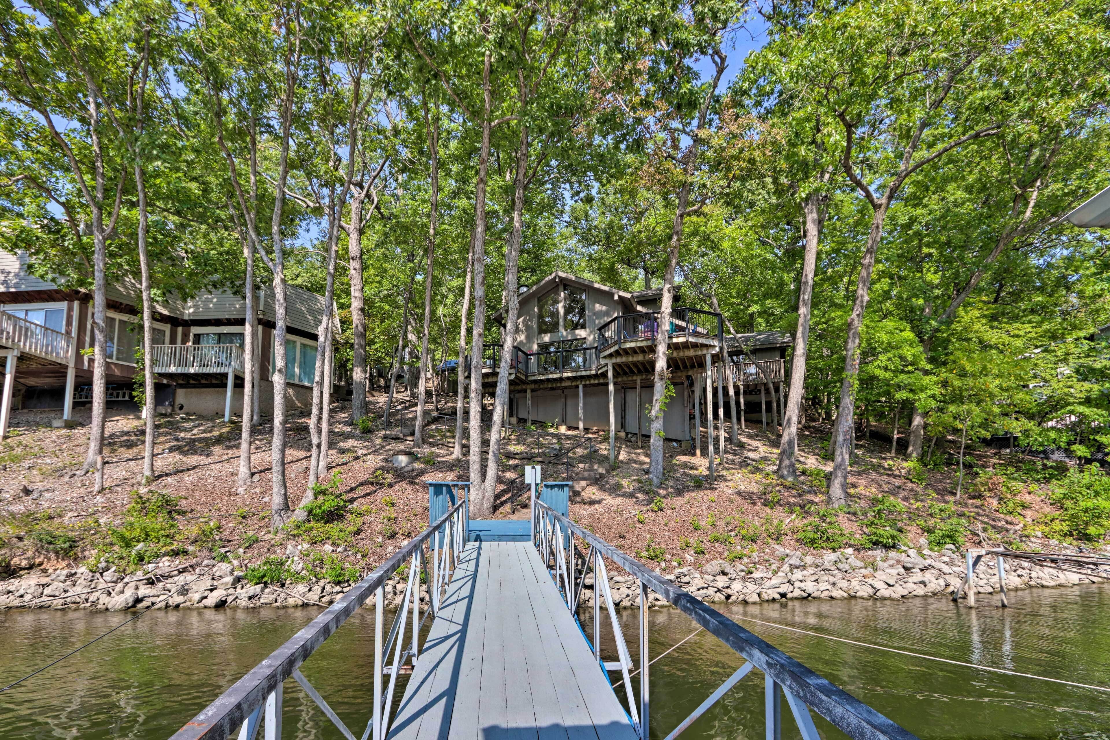 A wooden dock leading to a house surrounded by tall trees.