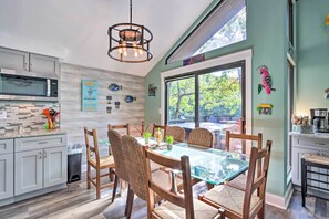 A modern kitchen with a dining area, featuring a large window, wooden chairs, and a hanging light fixture. - 2 Mi to Margaritaville: Lake of the Ozarks Home! (Osage Beach)
